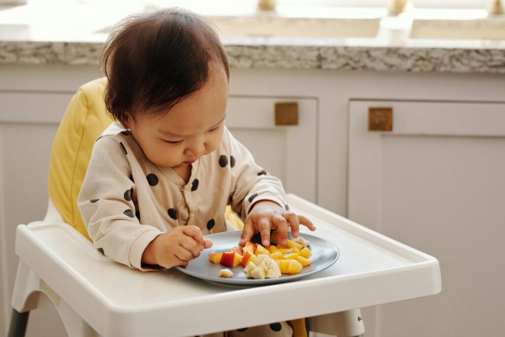 pexels-photo-5083240-5083240 A cute toddler in a polka dot outfit enjoying a healthy fruit snack indoors.